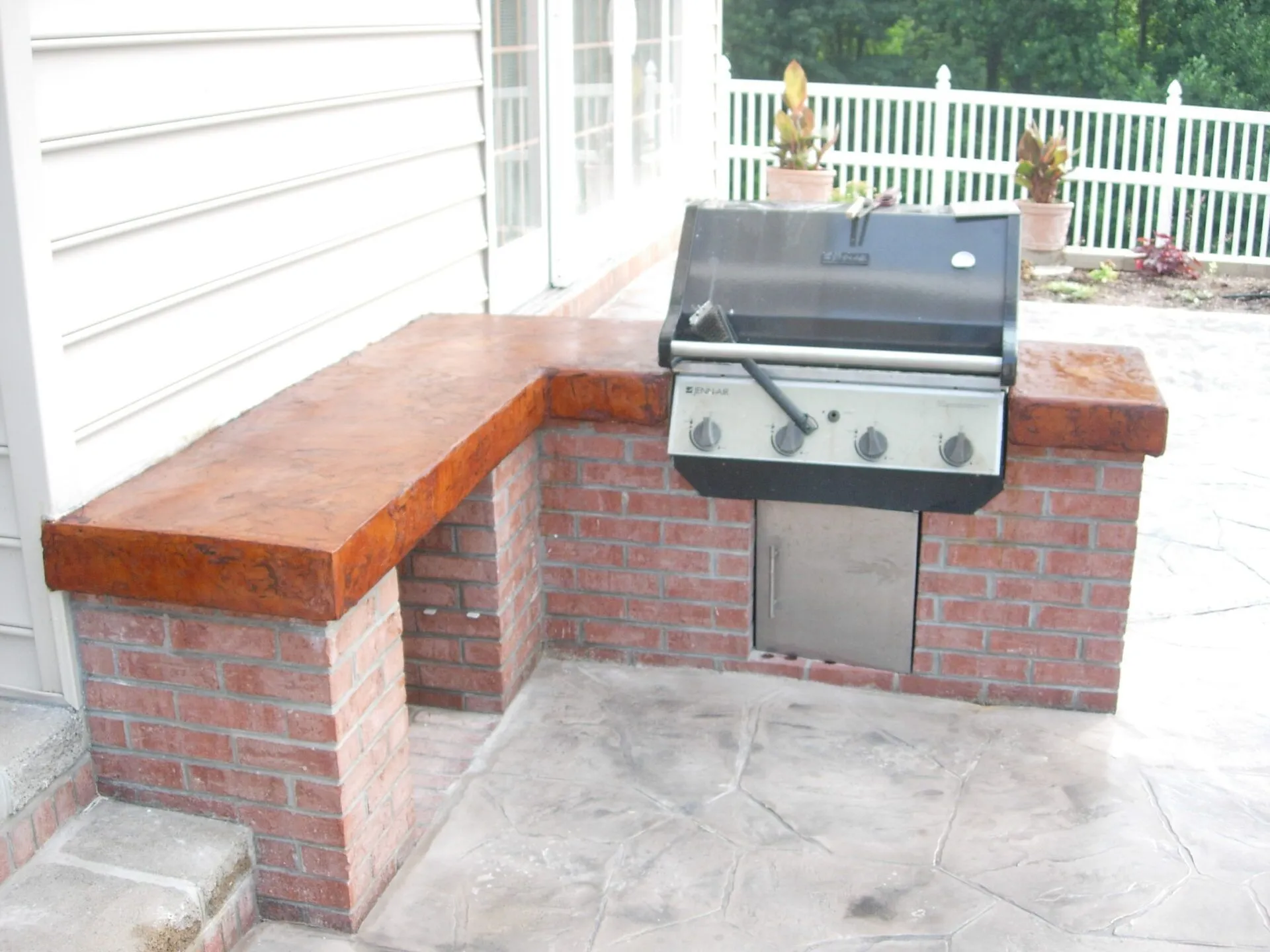 A grill is built into a brick wall on a patio with concrete floor