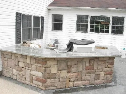 A stone counter with a grill on it in front of a house