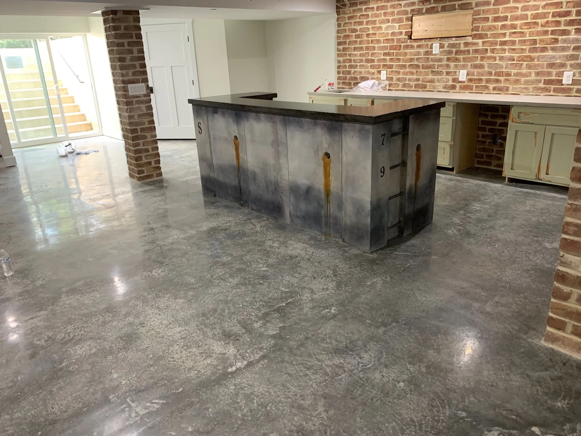 Concrete kitchen island on a polished grey concrete floor in a basement with brick walls